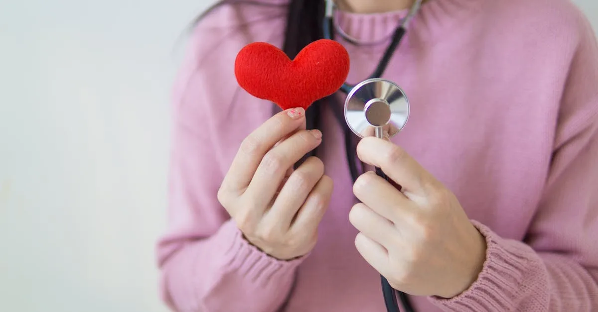 Person in a pink sweater holds a red plush heart with a stethoscope, symbolizing heart health.