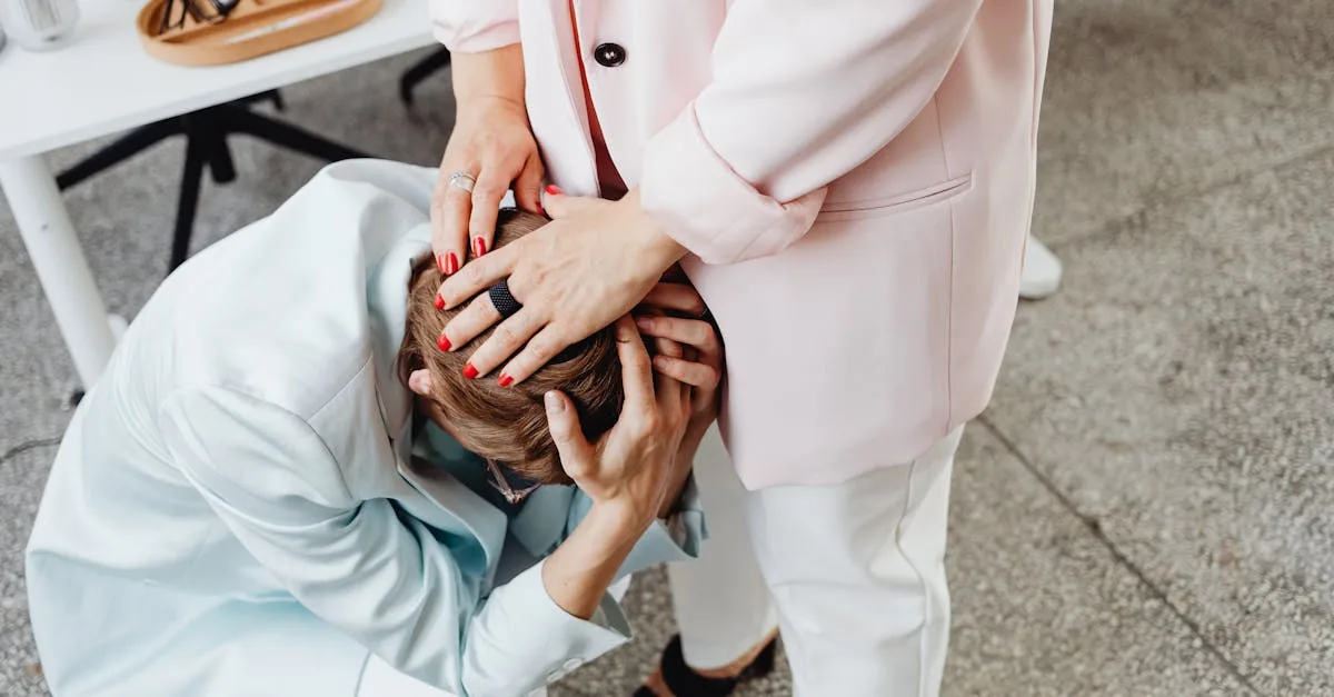 Caregiver or friend comforts someone who is leaning forward, hands cradling their head in a supportive gesture.