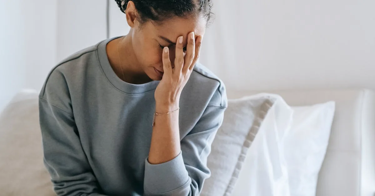 Woman sitting on a bed, head bent, hand covering her face in a moment of distress.