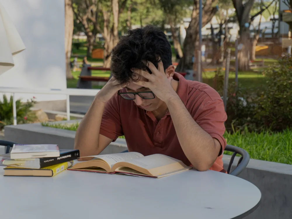 Guy holding his head, reading a book.